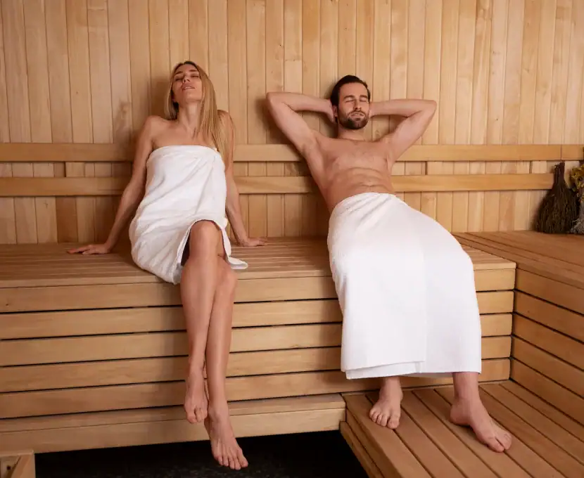 Relaxing man and woman sitting in a sauna with towels wrapped around their bodies.