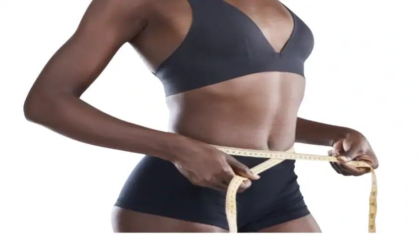 Slim woman measuring her waist with a tape measure, wearing black sportswear.