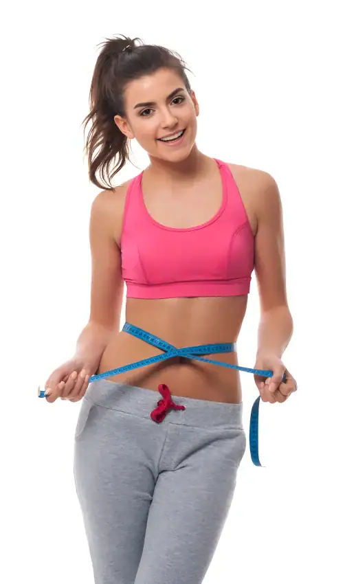 A woman in a pink sports bra and gray sweatpants measuring her waist with a blue tape.