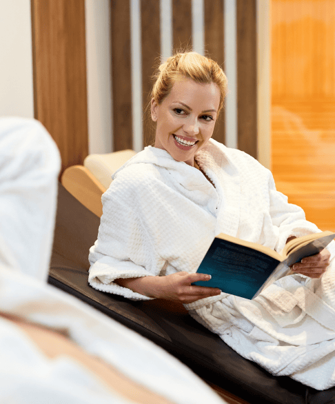 Relaxed woman in a white bathrobe reading a book in a spa or wellness center.