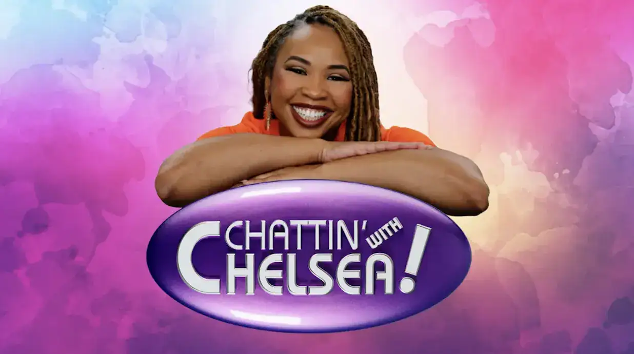 A woman with long braided hair smiling and resting her arms on a purple sign that says "Chattin' wit.