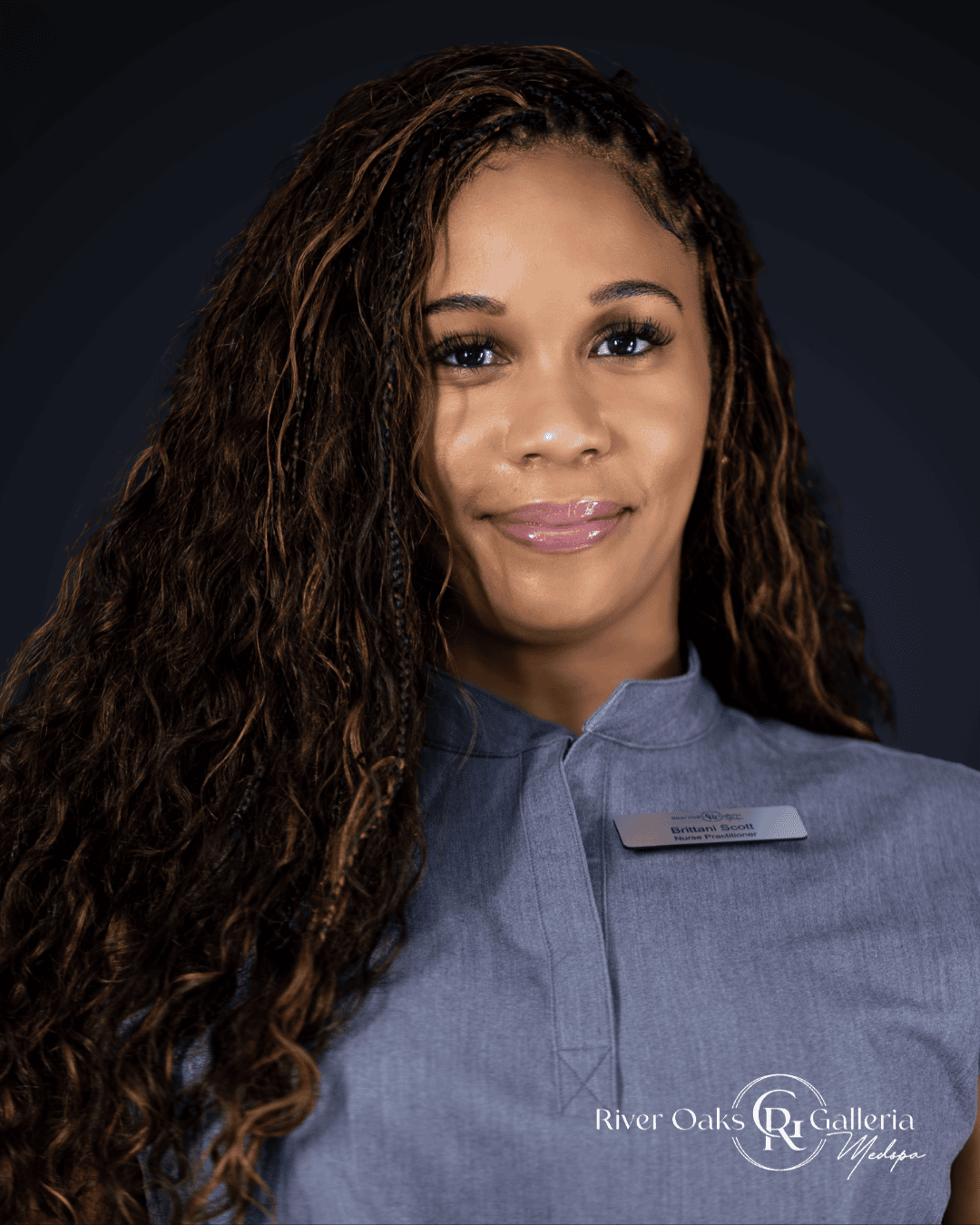 Woman with curly hair in a blue uniform, smiling, at River Oaks Galleria.